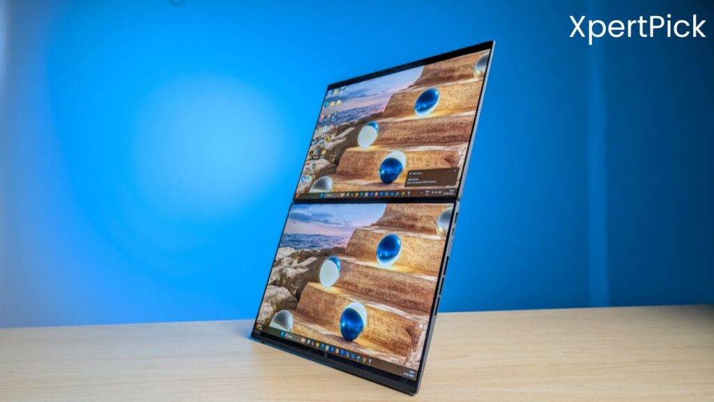 ASUS ZenBook Duo laptop shown in an angled view with its dual-screen setup active, placed on a wooden desk against a blue background. (Source: Yetnesh Dubey / XpertPick)