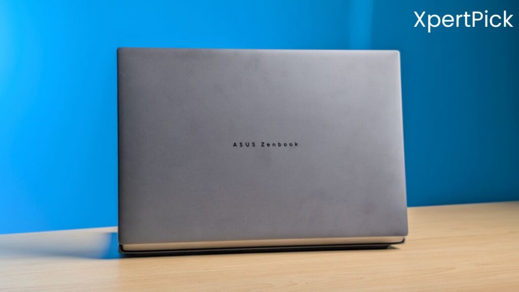 Rear view of the ASUS ZenBook Duo with a clean matte finish and subtle ASUS ZenBook branding on the lid, placed on a wooden desk against a blue background. (Source: Yetnesh Dubey / XpertPick)